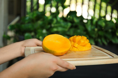 Woman holding wooden board with cut ripe mango outdoors, closeupの写真素材