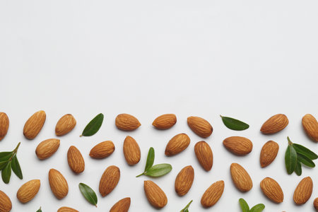 Delicious almonds and fresh leaves on white background, flat lay. Space for textの写真素材