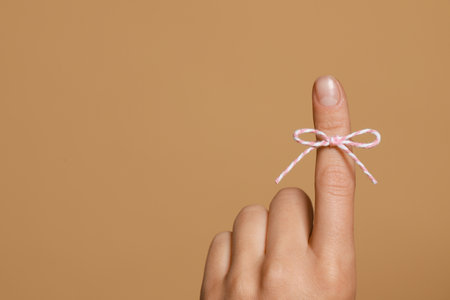 Woman showing index finger with tied bow as reminder on light brown background, closeup. Space for textの写真素材