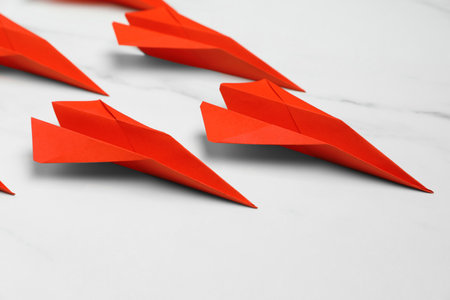 Many handmade paper planes on white marble table, closeup