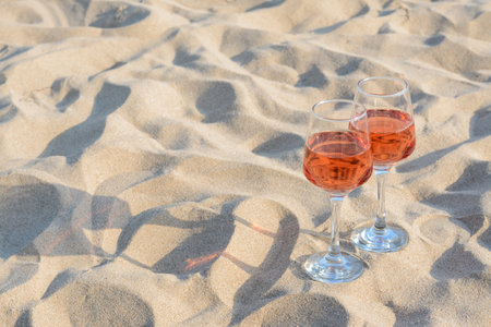 Glasses of tasty rose wine on sand, space for textの写真素材