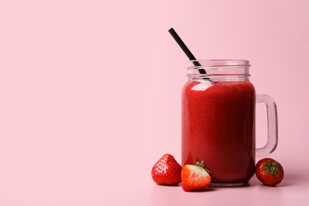 Mason jar with delicious berry smoothie and fresh strawberries on pink background. Space for textの写真素材