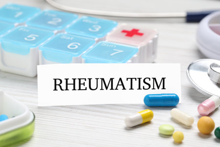 Card with word Rheumatism and pills on white wooden tableの写真素材
