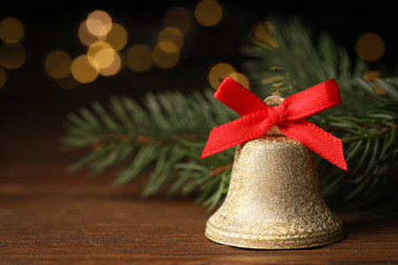 Bell with red bow and fir branches on wooden table against blurred background, closeup. christmas decorの写真素材