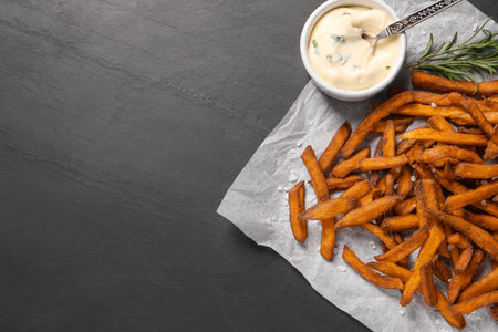 Delicious sweet potato fries and sauce on black table, top view. Space for textの写真素材