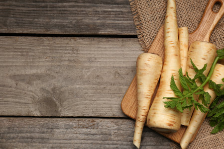 Many fresh ripe parsnips and green leaves on wooden table, flat lay. Space for textの写真素材