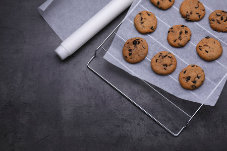 Roll of parchment baking paper and cooling rack with tasty cookies on dark gray table, flat lay. Space for textの写真素材