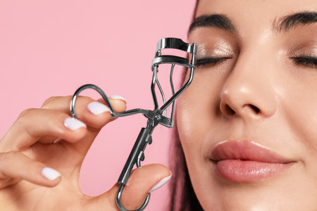 Young woman using eyelash curler on light pink background, closeupの写真素材