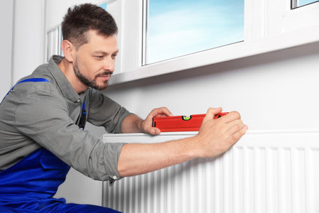 Professional plumber using bubble level for installing new heating radiator in roomの写真素材