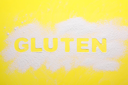 Word Gluten written with flour on yellow background, top viewの写真素材