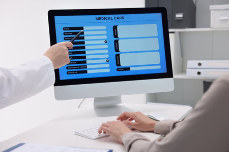 Doctor using computer to fill out patient's medical card at table in clinic, closeup
