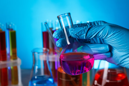 Scientist holding flask with liquid on light blue background, closeup