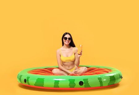 Happy young woman with sunscreen bottle on inflatable mattress against orange background. Seasonal suntanの写真素材