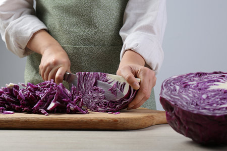 Woman cutting fresh radicchio cabbage on board at wooden table, closeupの写真素材