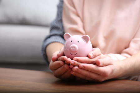 Couple with piggy bank at wooden table, closeupの写真素材
