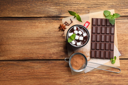 Mug of delicious hot chocolate with marshmallows and fresh mint near ingredients on wooden table, top view. Space for textの写真素材