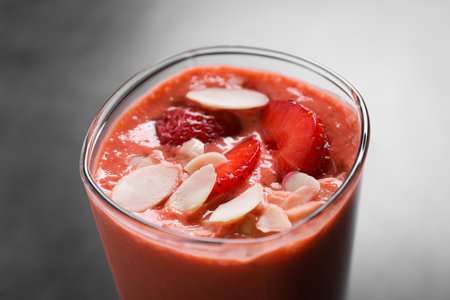 Glass of delicious smoothie with strawberry and almond flakes on gray table, closeupの写真素材