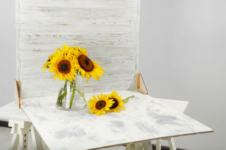 Glass vase with beautiful sunflowers and double-sided backdrop on table in photo studioの写真素材
