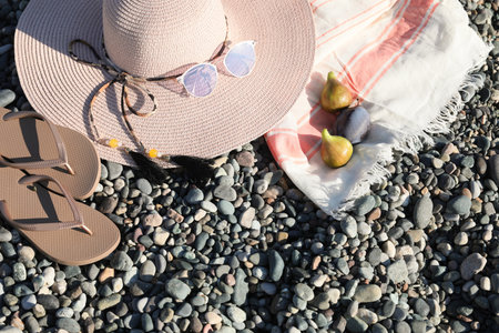 Beautiful hat with sunglasses and flip flops on pebbles, flat lay. Space for text