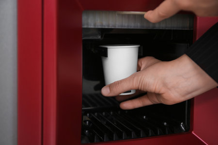 Woman taking paper cup with coffee from vending machine, closeup
