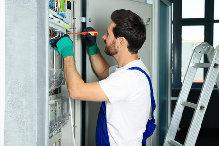 Electrician repairing fuse box with screwdriver indoors