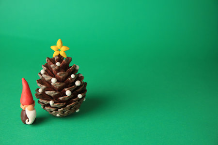 Beautiful plasticine dwarf with pinecone on green background, space for text. Children's handmade ideasの写真素材