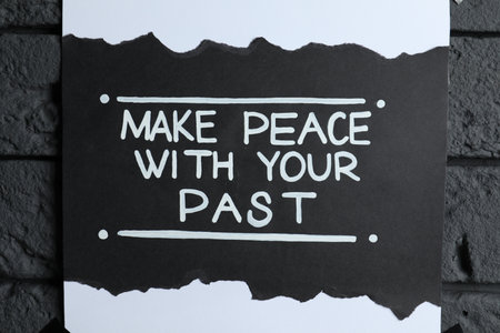 Card with life-affirming phrase Make Peace With Your Past on dark brick wall, closeupの写真素材