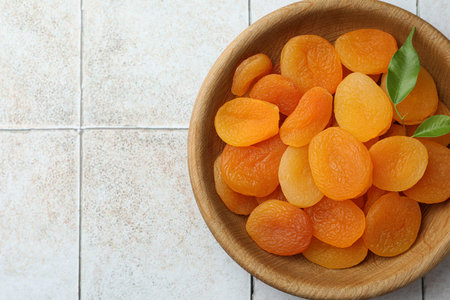 Wooden bowl of tasty apricots and space for text on white tiled table, top view. dried fruitsの写真素材