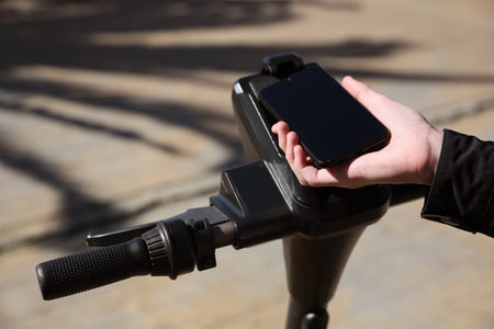 Man using smartphone to pay and unblock rental electric scooter outdoors, closeupの写真素材