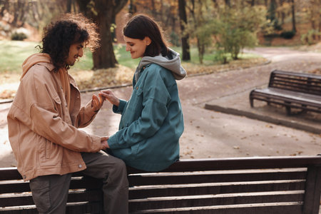 Happy young couple spending time together on wooden bench in autumn park, space for text. dating agencyの写真素材
