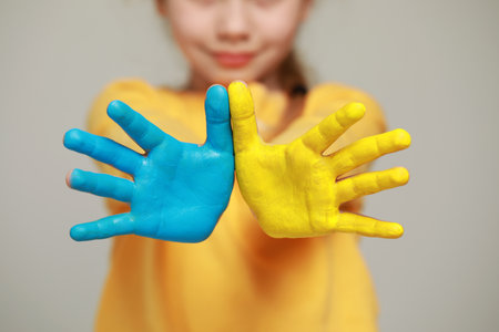 Little girl with hands painted in Ukrainian flag colors against light gray background, closeup. love ukraine conceptの写真素材