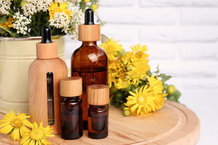Bottles of essential oil and different wildflowers on wooden board, space for textの写真素材