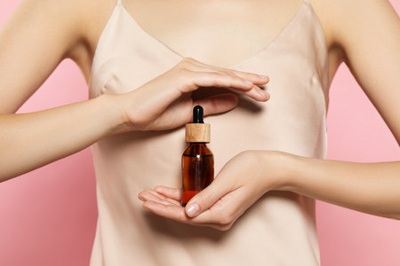 Young woman with bottle of essential oil on pink background, closeupの写真素材