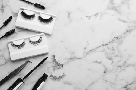 Flat lay composition with false eyelashes and tools on white marble table. Space for textの写真素材