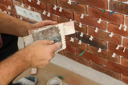 Professional builder applying cement onto decorative brick near wall, closeup. Tiles installation processの写真素材