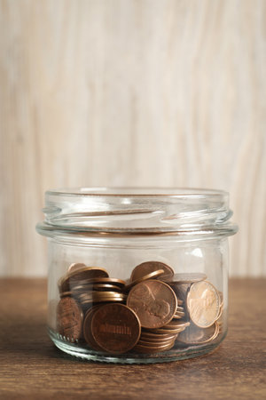 Glass jar with coins on wooden table, closeup