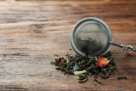 Snap infuser with dried herbal tea leaves on wooden table, closeup. Space for textの写真素材