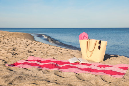 Towel with book and beach accessories on sand near sea, space for textの写真素材
