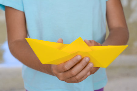 Little girl holding yellow paper boat outdoors, closeupの写真素材