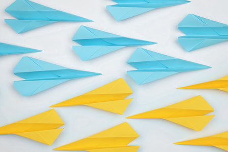 Handmade paper planes in light blue and yellow colors on white table, flat lay
