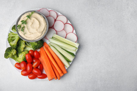 Plate with delicious hummus and fresh vegetables on light gray table, top view. Space for textの写真素材