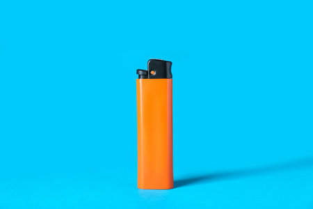 Orange plastic cigarette lighter on light blue backgroundの写真素材