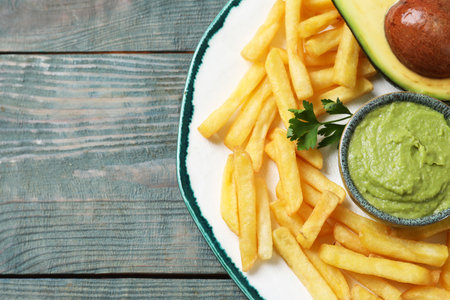 Plate with french fries, guacamole dip, parsley and avocado served on gray wooden table, top view. Space for textの写真素材