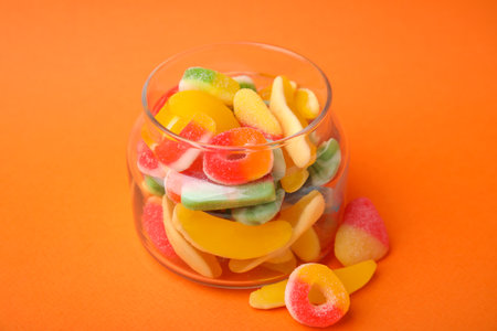 Tasty jelly candies in jar on orange background, closeup