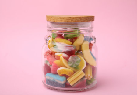 Tasty colorful candies in glass jar on pink backgroundの写真素材