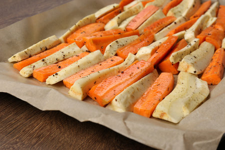 Baking tray with parchment, parsnips and carrots on wooden table, closeupの写真素材