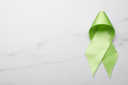 World Mental Health Day. Green ribbon on white marble table, top view with space for textの写真素材
