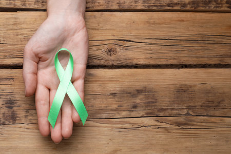 World Mental Health Day. Woman holding green ribbon on wooden background, top view with space for textの写真素材