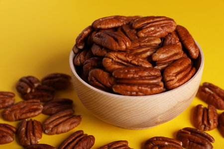 Tasty pecan nuts with bowl on yellow background, closeupの写真素材
