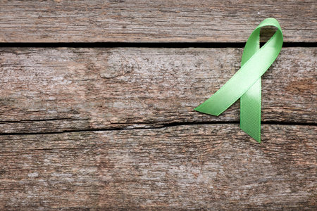 World Mental Health Day. Green ribbon on wooden background, top view with space for textの写真素材
